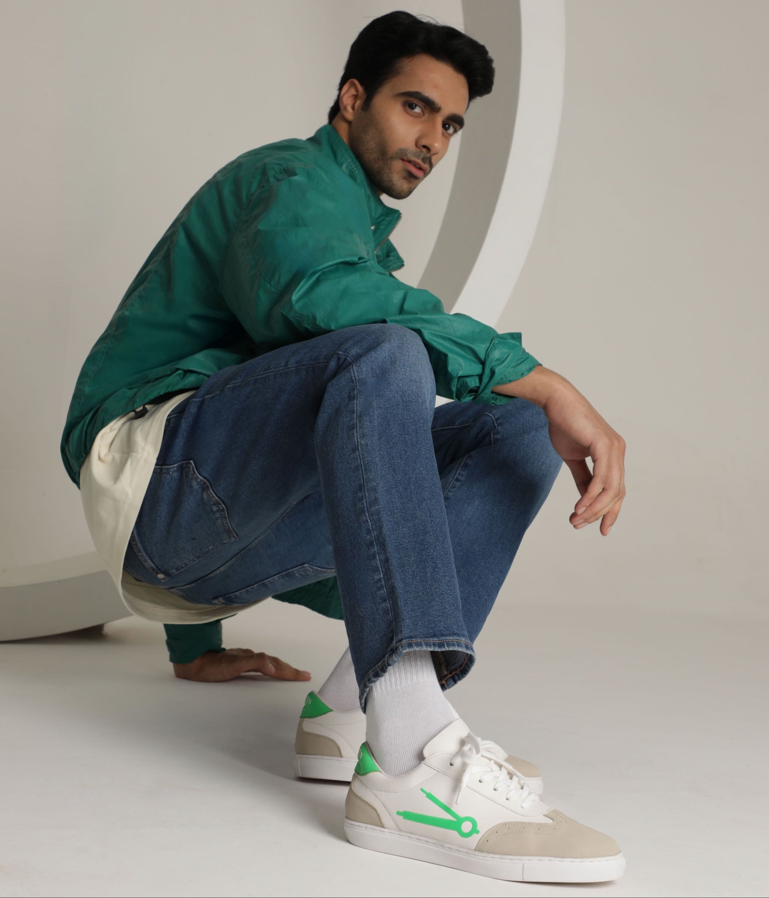 Man in green jacket and jeans sitting on a white surface with a neutral background